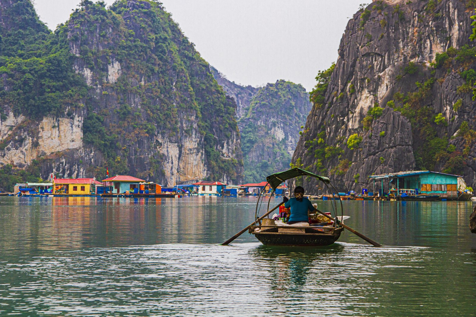 The image shows a fishing village in the famous Ha Long Bay surrounded by towering limestone islands which protect it from storms