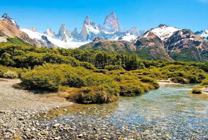 A glacier-fed lake with hikers walking the trail in front of snow-capped peaks in Patagonia: digital detox gateways