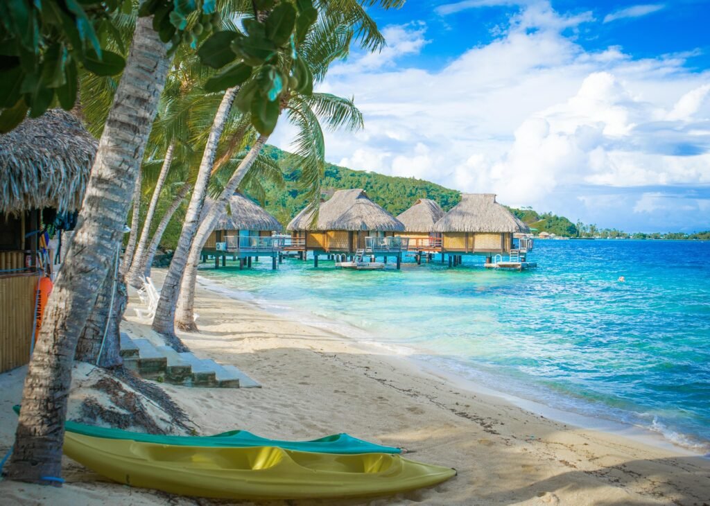 Overwater bungalows extend into the crystal-clear sea, framed by palm trees and a serene sandy shore.