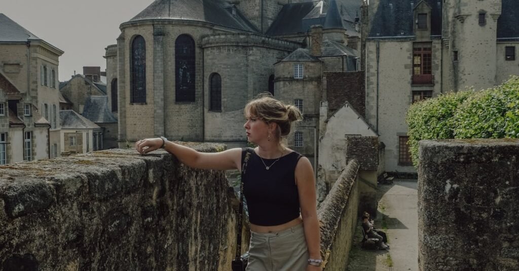 A woman stands on a stone walkway near a historic European building, showcasing classic architecture.