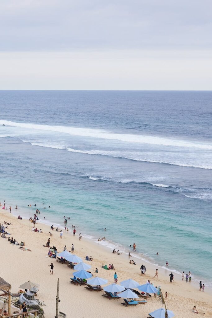 A vibrant beach in Bali, Indonesia with tourists enjoying under blue umbrellas.